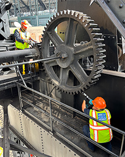 two workers greasing the giant gear on the third street bridge