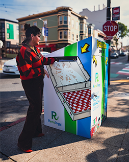 a woman putting an empty pizza box into a pizza box trash can