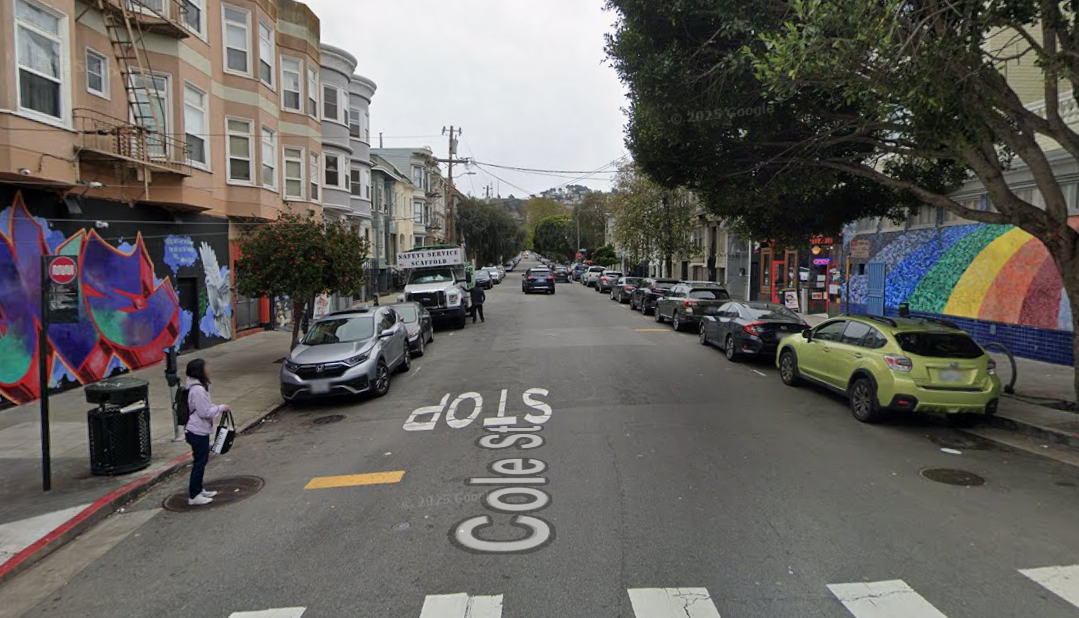 street level view of the Cole Street and Haight Street intersection looking south toward Waller Street. Depicted are the roadway with vehicles street parked on either side, as well as the buildings that line this block of Cole Street.