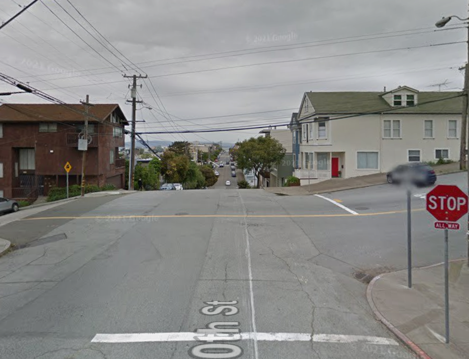 Street level photo of the intersection of 20th Street and De Haro Street, looking eastward down 20th Street. The intersection is shown in its current state, with cracked, uneven pavement.