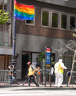 workers cleaning up the street. A rainbow flag flies above them.