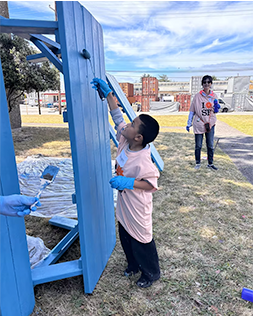 A boy putting a fresh coat of blue paint on a park table