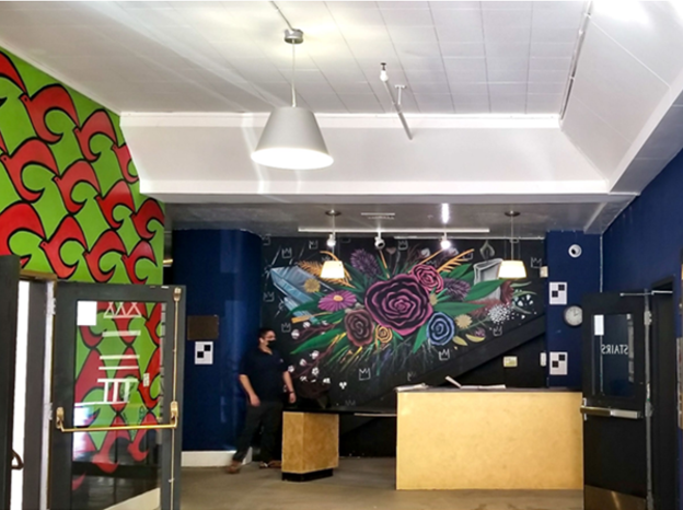 Interior view of the reception area of the African American Arts and Cultural Complex, including a reception desk in the foreground with a pink, blue and green floral mural painted on the back wall.